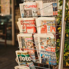 Stack of diverse newspapers in a metal stand, showcasing media variety.